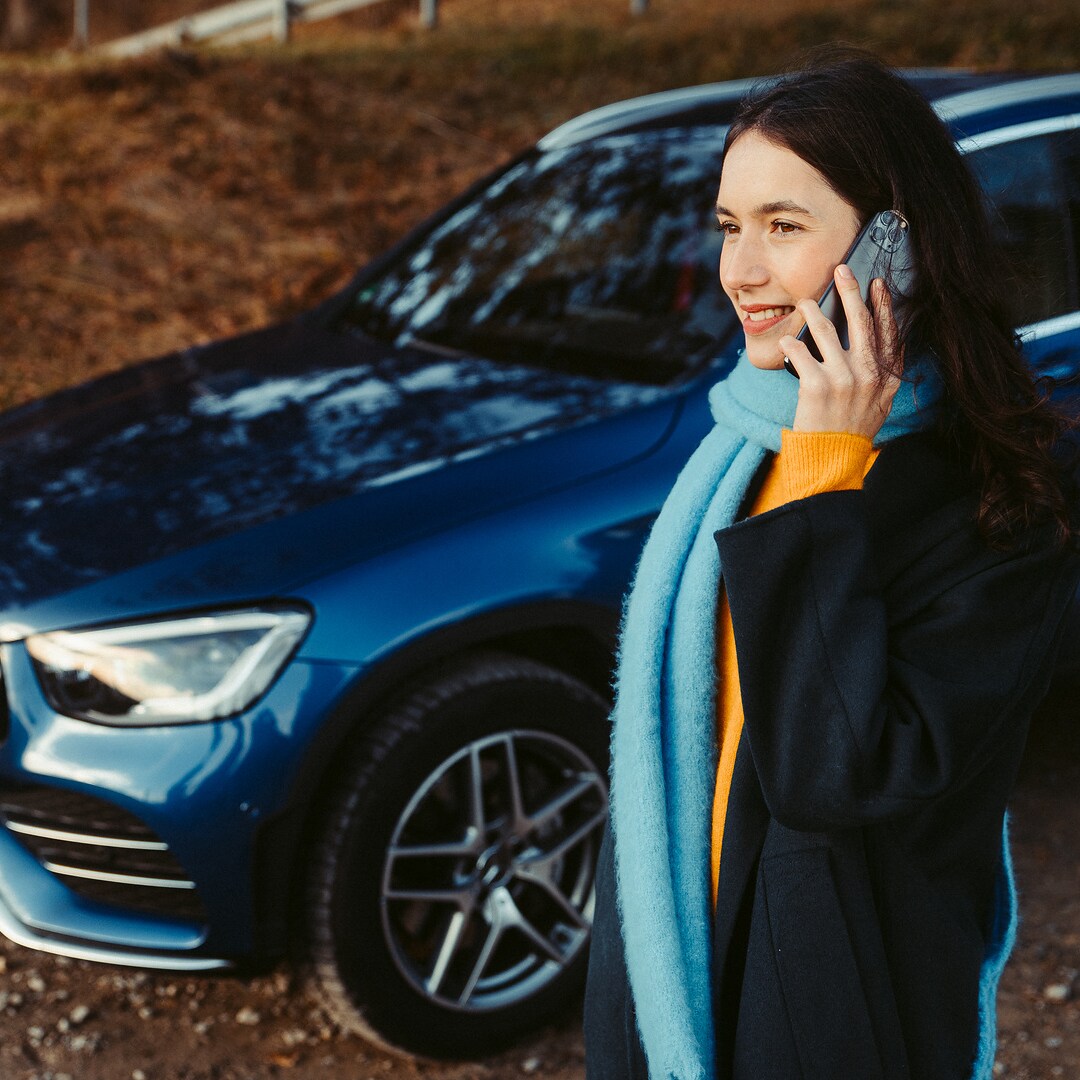 한 여성이 자신의 Mercedes SUV 앞에서 스마트폰으로 통화하고 있습니다.