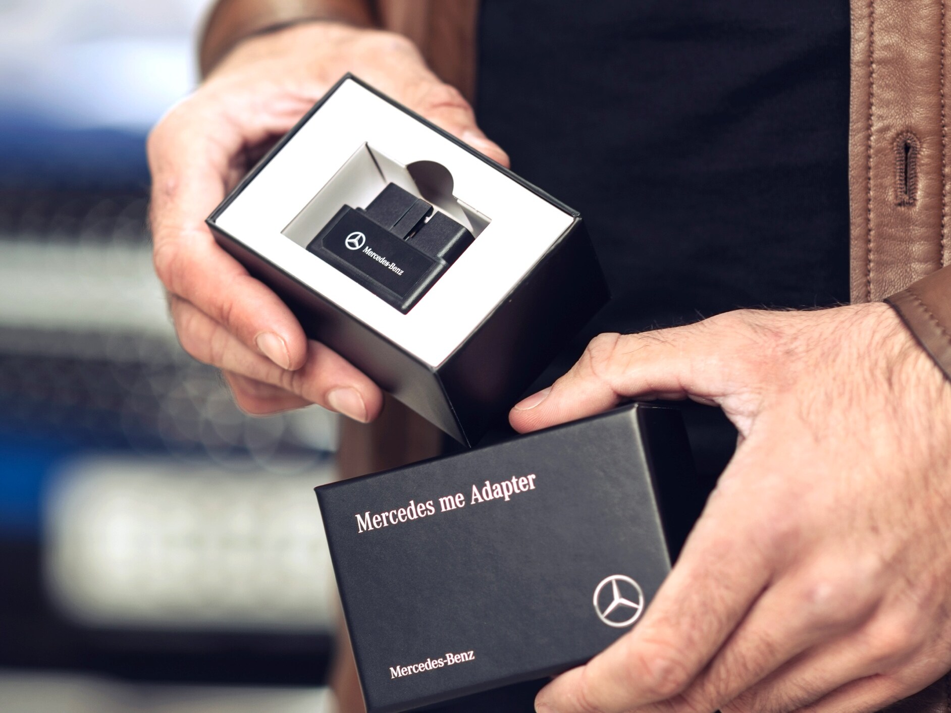 한 남성이 자신의 차량에서 디지털 서비스 상품을 사용하기 위해 메르세데스-벤츠용 Mercedes-Benz Adapter의 포장을 풀고 있습니다.