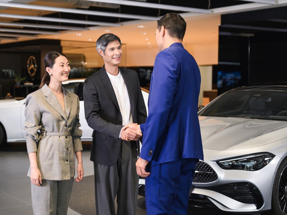 Man and woman sitting in blue Mercedes-Benz EQS with dealer showing vehicle features