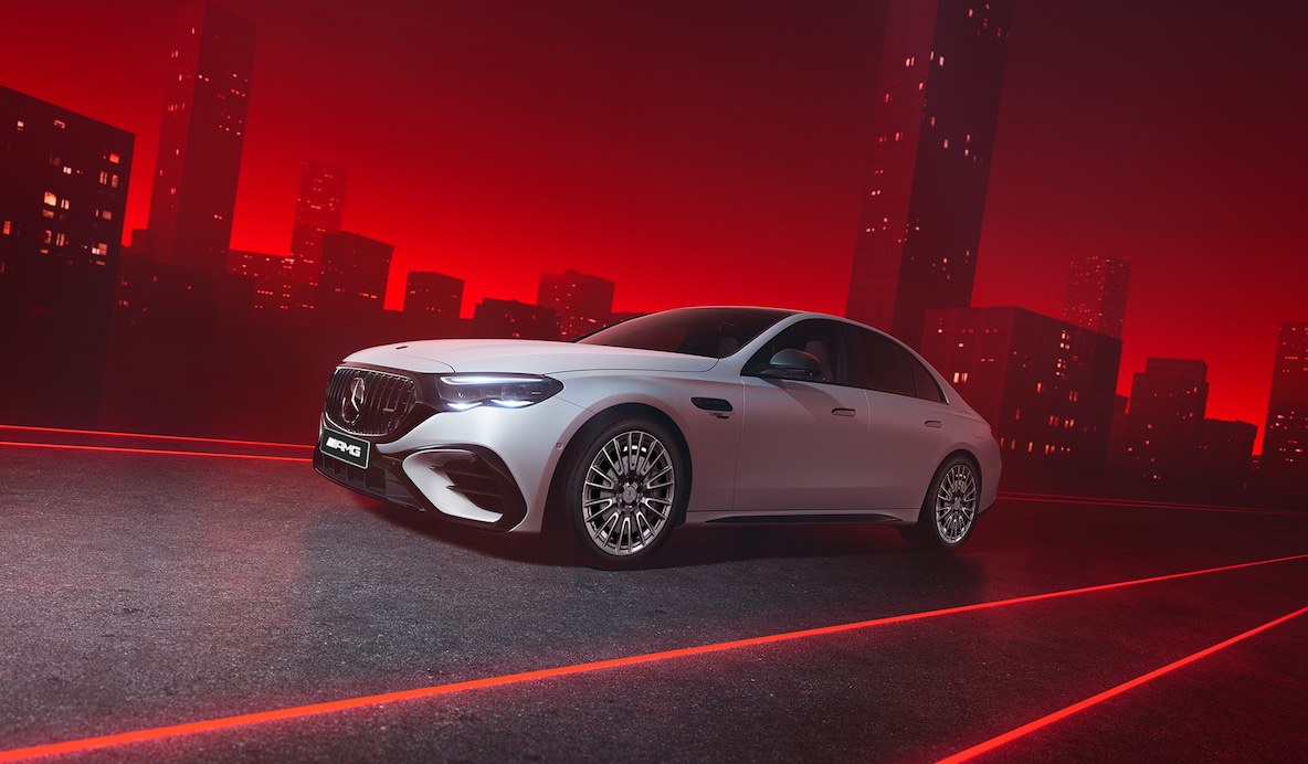 빨간색 배경에 서 있는 Mercedes-AMG E 53 HYBRID 4MATIC+의 전면을 위에서 바라본 모습.